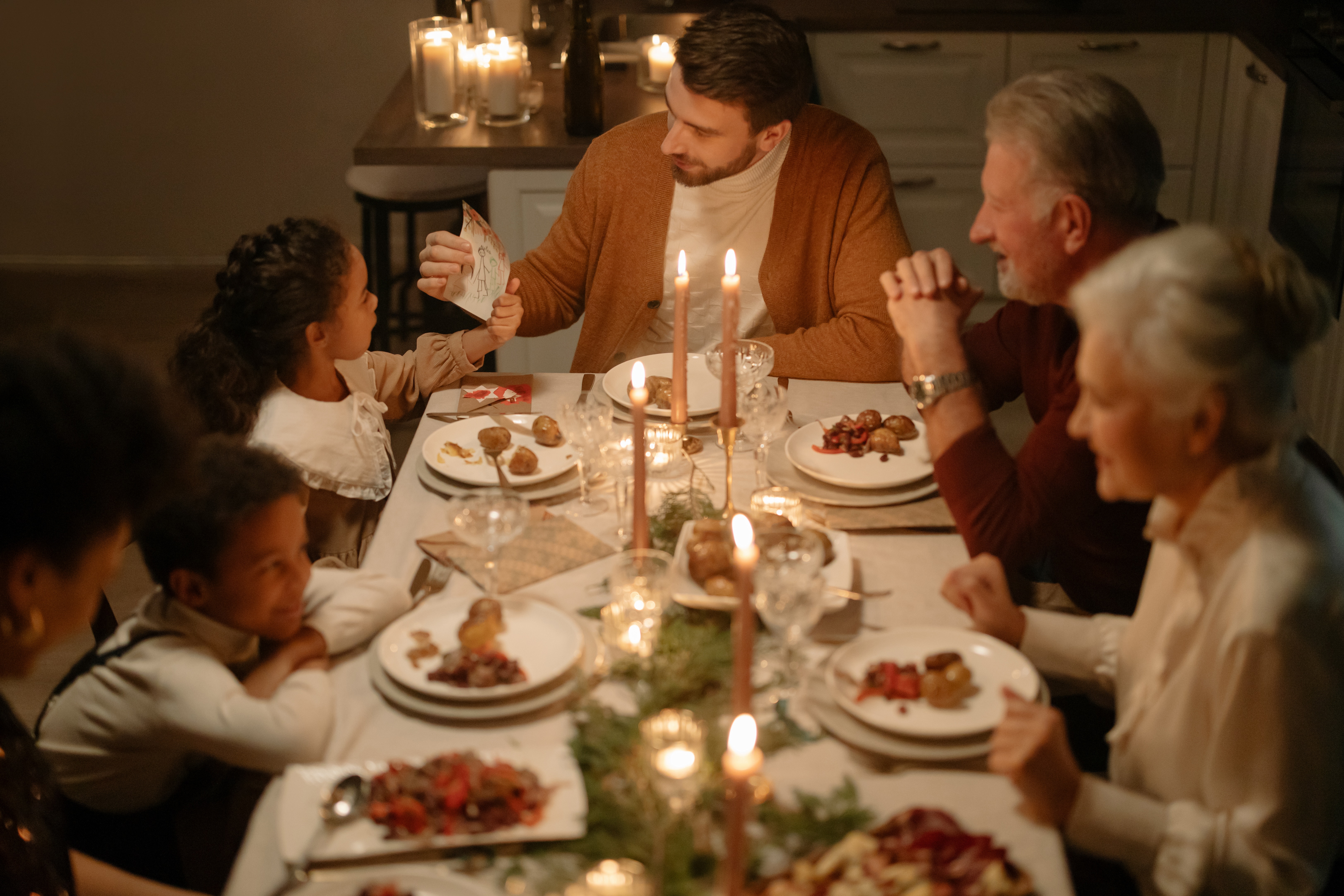 Family gathered at holiday themed dinner table with candles. 