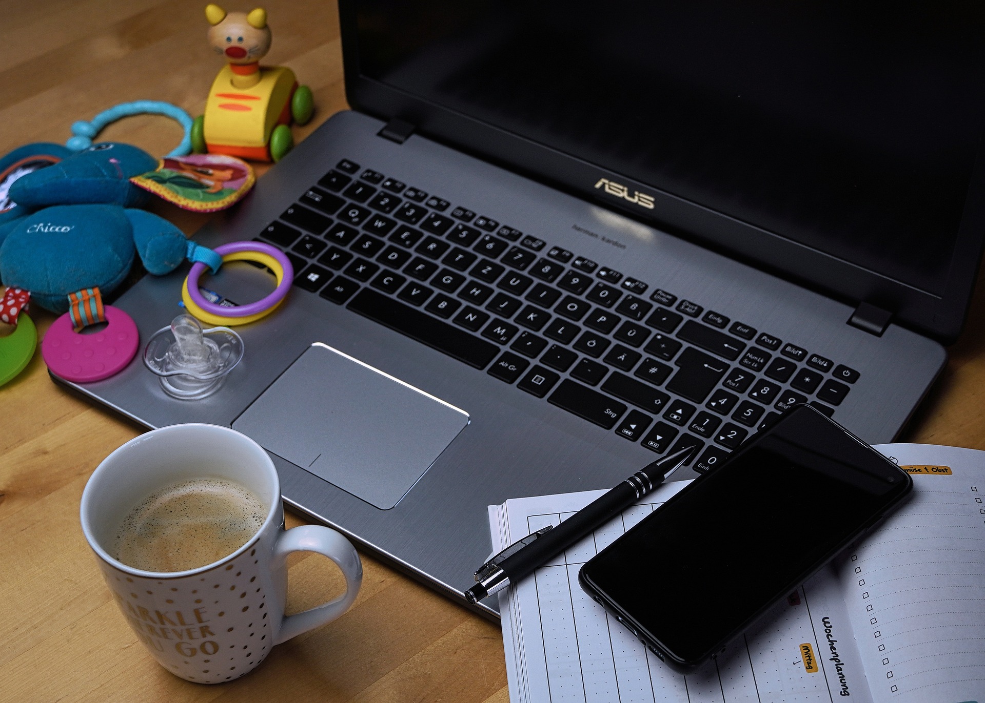 Laptop on a desk with a coffee cup and children's toys to show work-from-home and work-life balance.