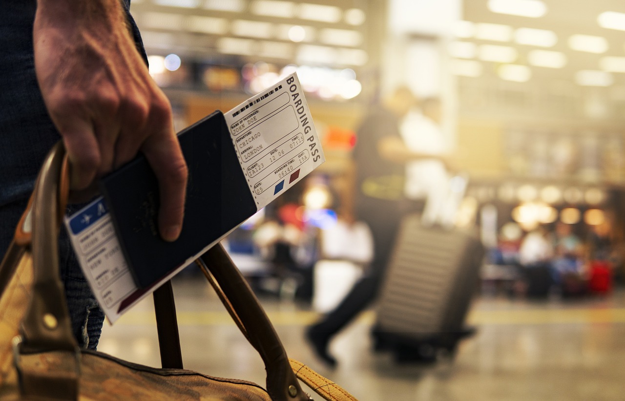 Close up of a hand holding a boarding pass and a bag with a blurred airport in the background