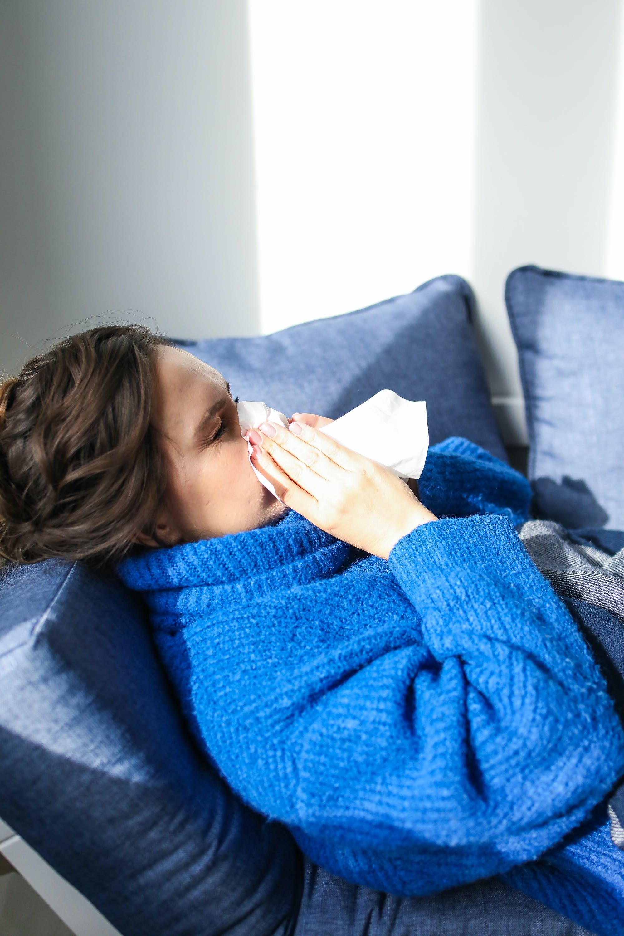 stock image of a woman who is sneezing or coughing into a tissue