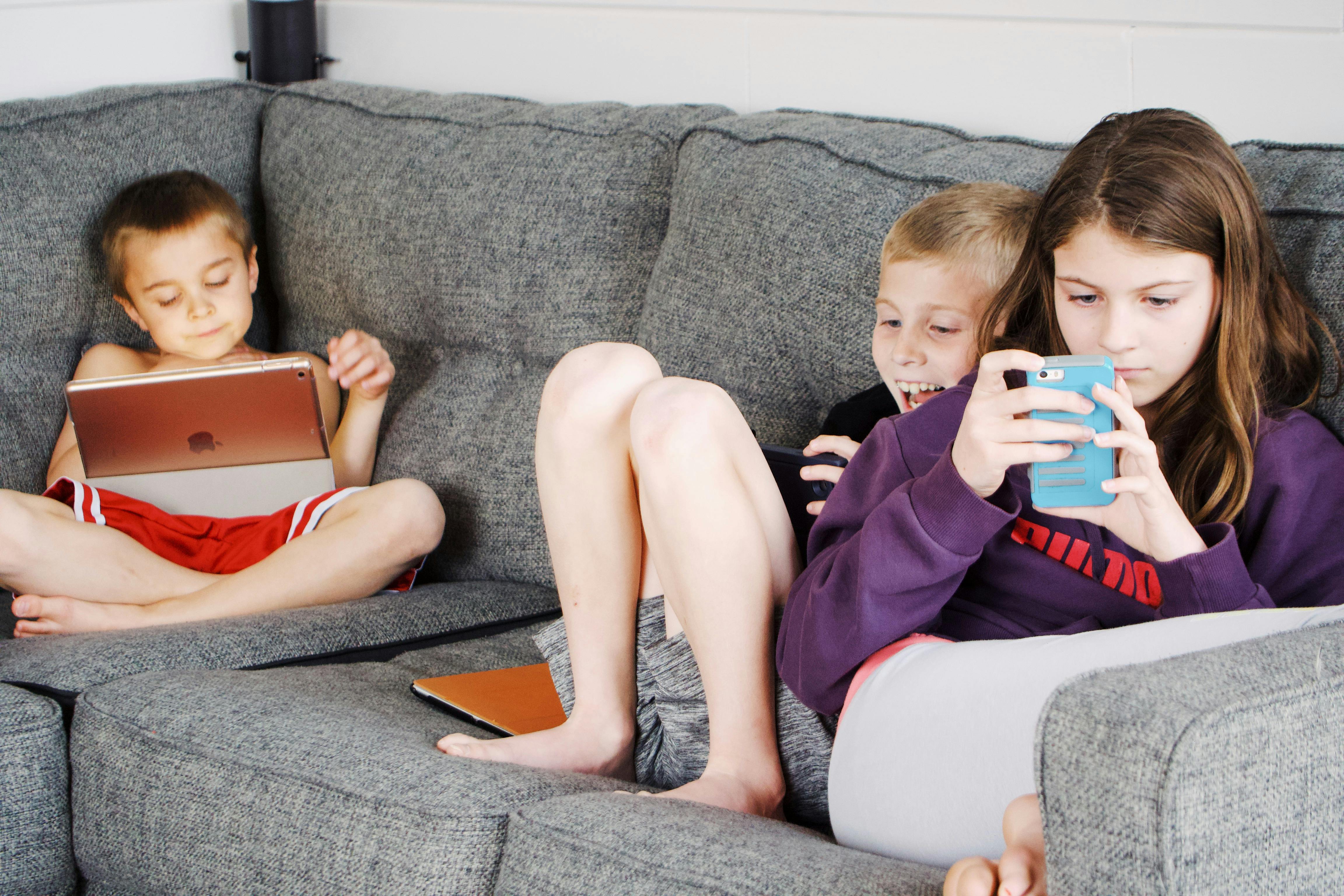 kids sitting on a couch with phones and tablets