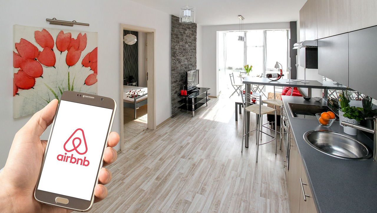 hand holding a phone with the Airbnb logo with a kitchen in the background