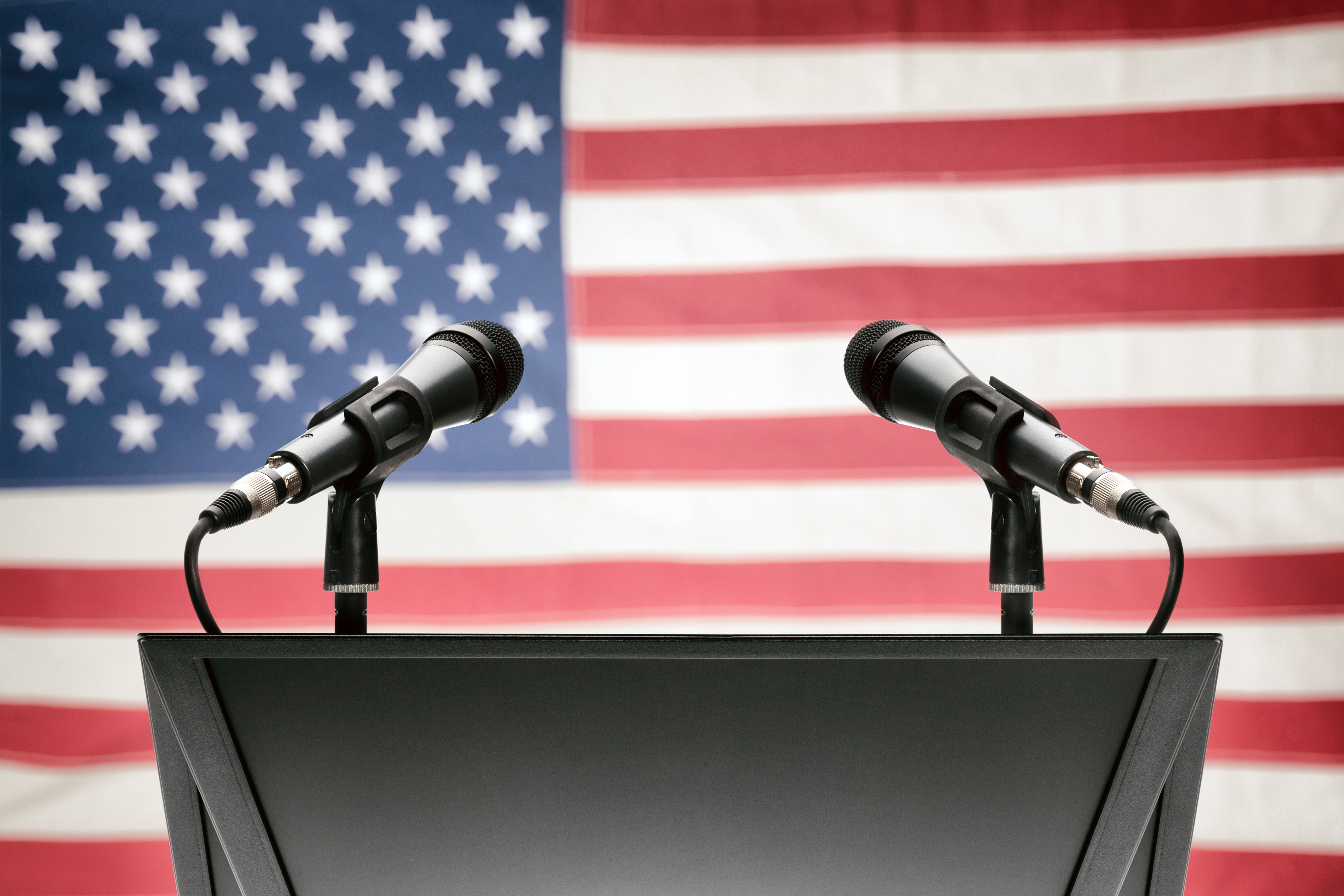 two microphones on a lectern with the American flag in the backgrounf