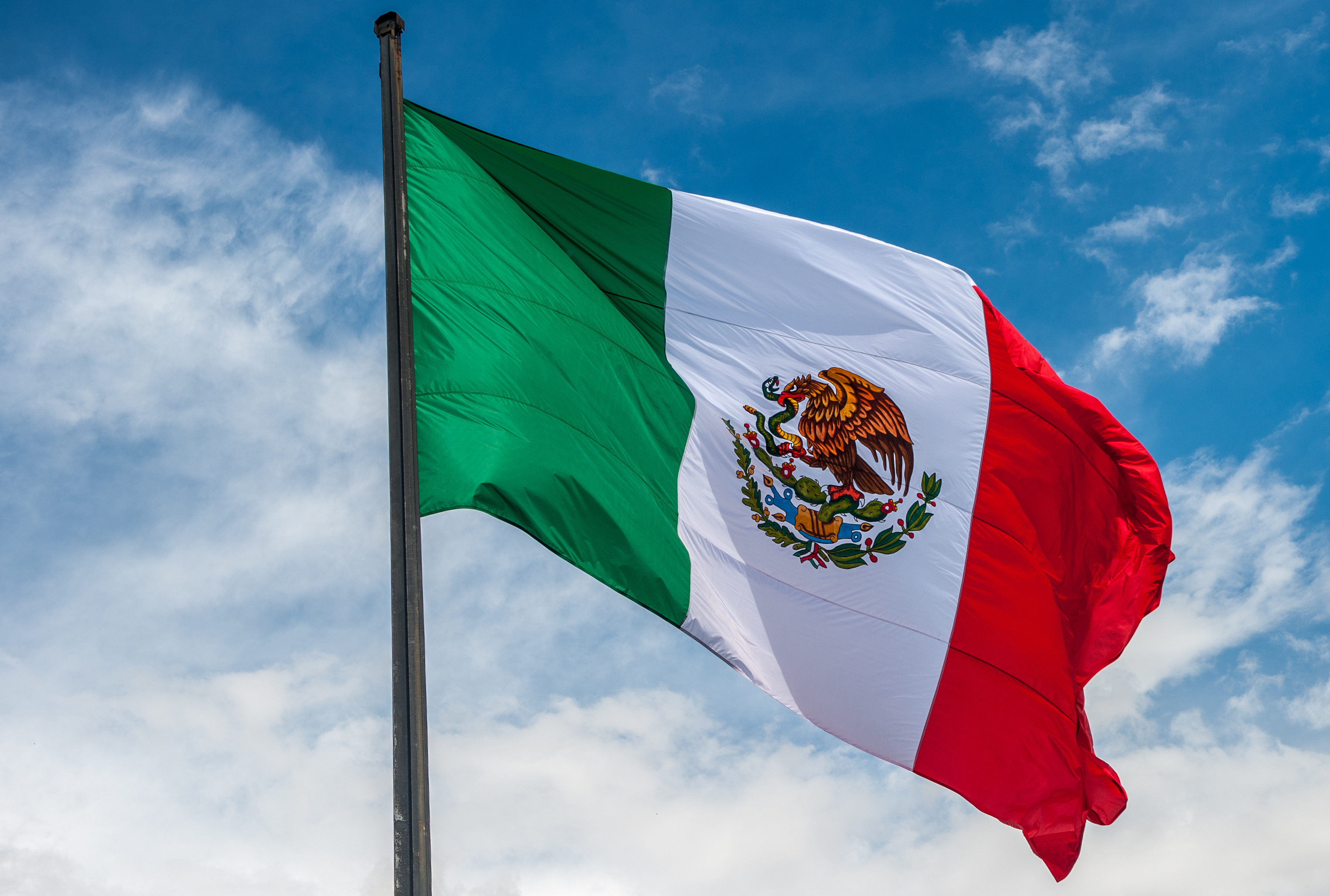 Mexico Flag flying on a flag pole with a blue sky in the backgroun