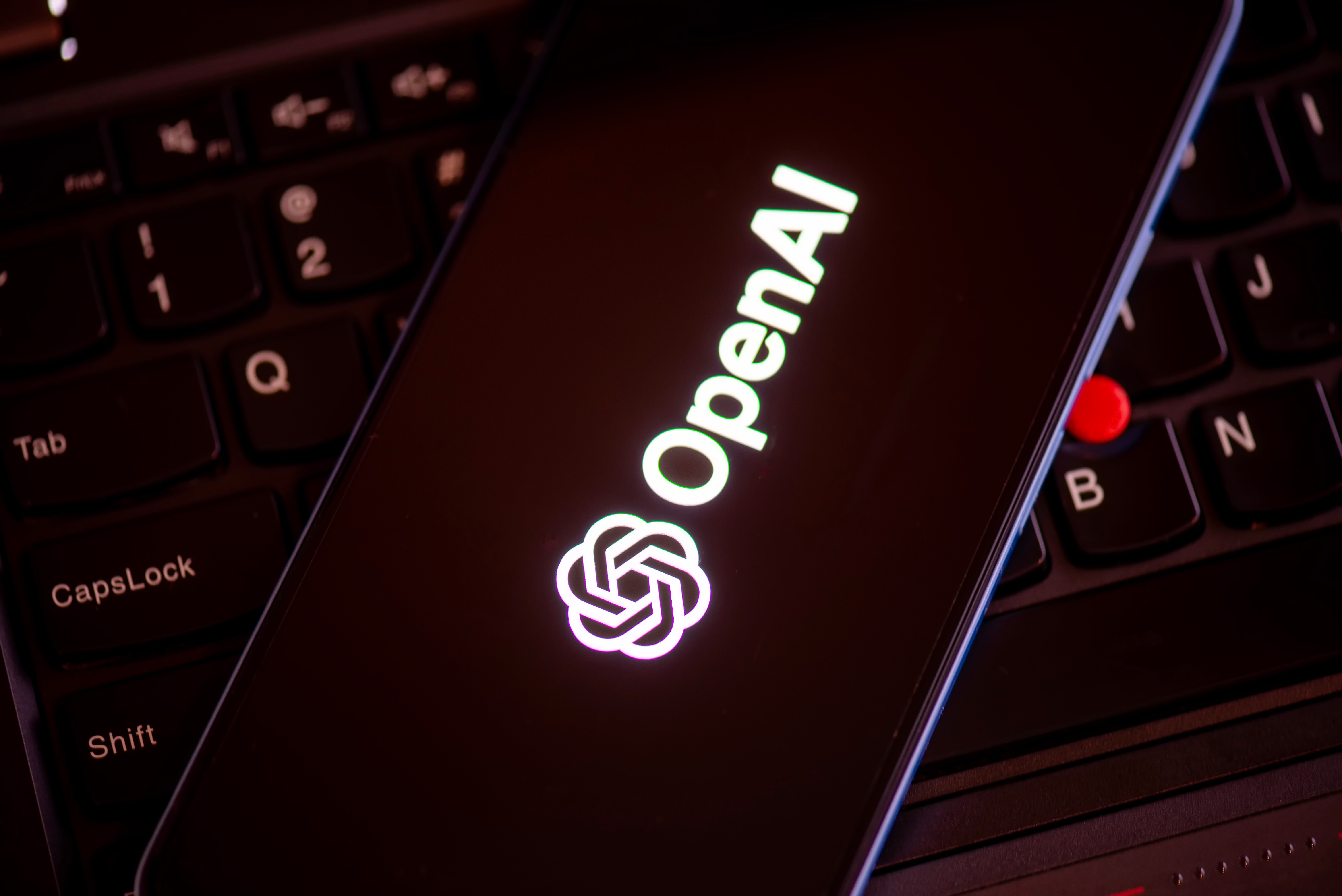 OpenAI logo on a phone screen with a computer keyboard in the background