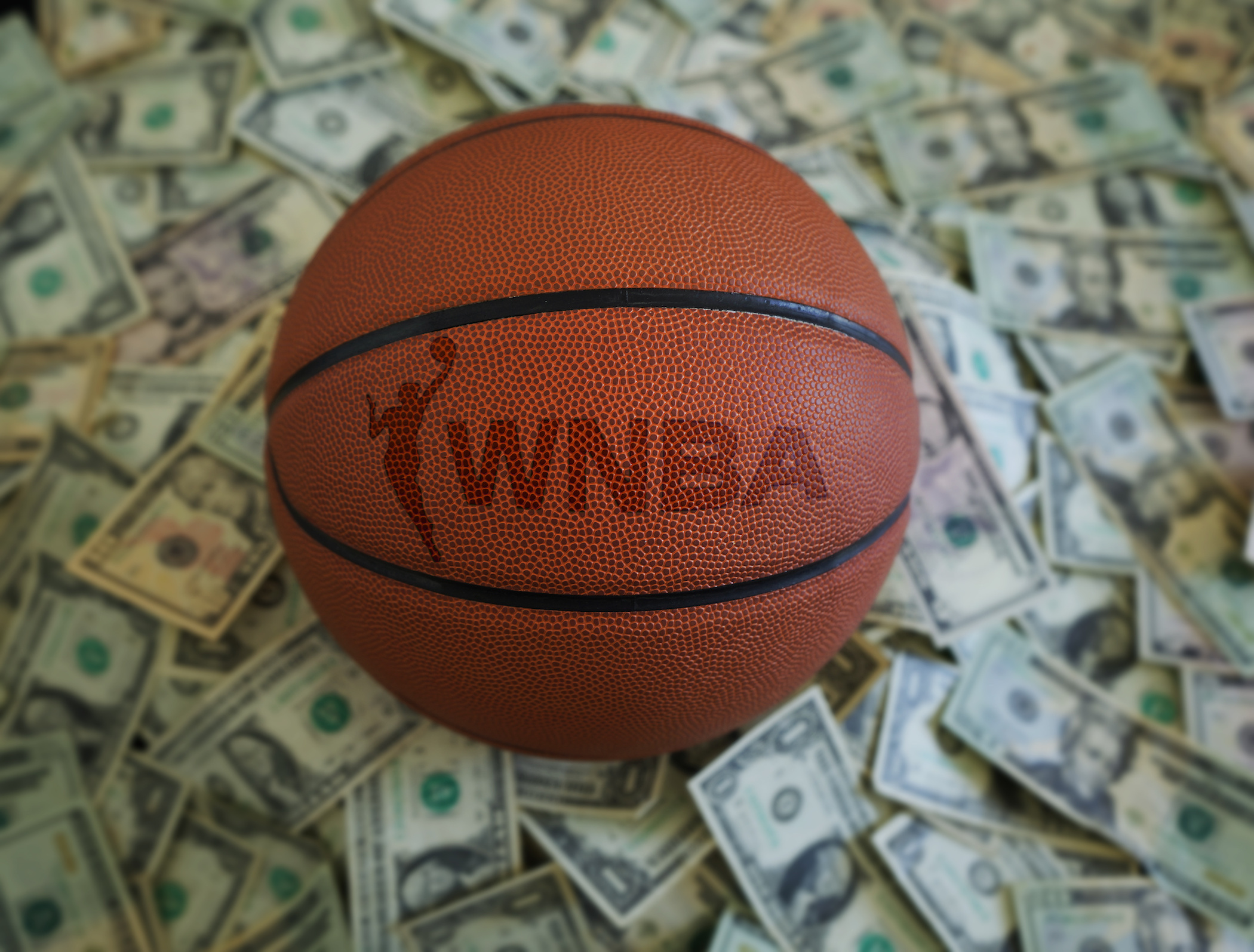 WNBA logo on a basketball with money in the background