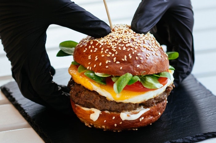 A cheeseburger held by hands with plastic gloves