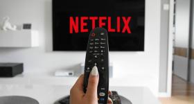 someone off camera holding a remote in front of a TV screen that reads "Netflix"