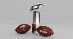 Two footballs laying next to a trophy