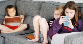 kids sitting on a couch with phones and tablets
