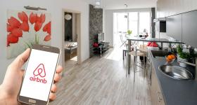 hand holding a phone with the Airbnb logo with a kitchen in the background
