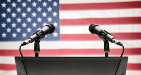 two microphones on a lectern with the American flag in the backgrounf