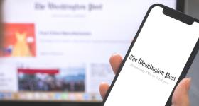 Washington Post logo on a phone screen with the website in the background